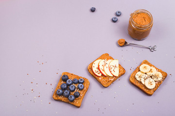 Sandwiches with peanut butter and fruits and seeds on a gray background. Healthy vegetarian breakfast. Top view, flat lay, copy space.