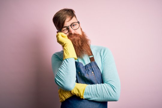 Irish redhead housekeeping man with beard wearing apron and washing gloves thinking looking tired and bored with depression problems with crossed arms.