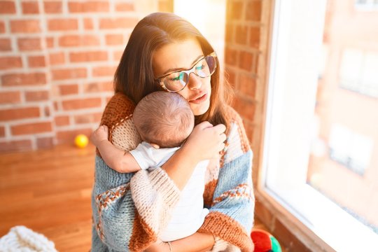 Young beautifull woman and her baby standing at home. Mother holding and hugging newborn