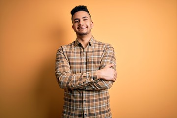 Young handsome man wearing casual shirt standing over isolated yellow background happy face smiling with crossed arms looking at the camera. Positive person.