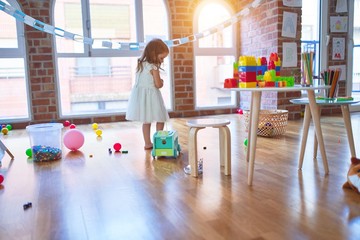 Adorable blonde toddler playing with car around lots of toys at kindergarten