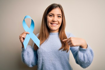 Young blonde woman holding prostate cancer awareness campaing blue ribbon with surprise face pointing finger to himself