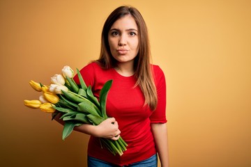 Young blonde woman holding romantic bouquet of tulips flowers over yellow background looking at the camera blowing a kiss on air being lovely and sexy. Love expression.