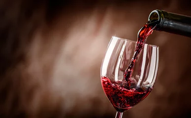  Pouring red wine into the glass against rustic background. © Milan