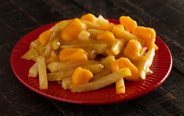 Plate of Poutine with Orange Cheddar Cheese with Brown Gravy on French Fries