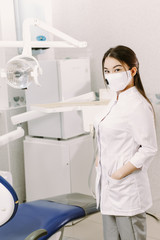 Cheerful female dentist smiling at her office. Beautiful woman student in a protective mask in dentistry stands in the dental office