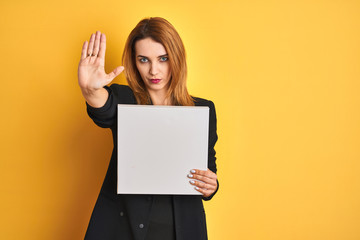 Naklejka premium Young redhead businesswoman with clear eyes holding banner over isolated yellow background with open hand doing stop sign with serious and confident expression, defense gesture