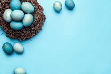 Easter eggs in nest on blue background. Flat lay, top view.
