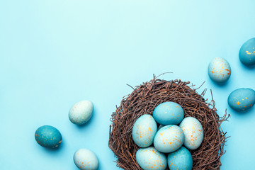 Easter eggs in nest on blue background. Flat lay, top view.