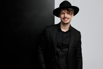 Positive fashion model smiling while wearing suit and hat, standing on black and white studio background