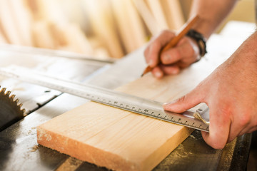 Fototapeta na wymiar Close up view of carpenter hands measure wooden board. Pencil and measuring tools detail.