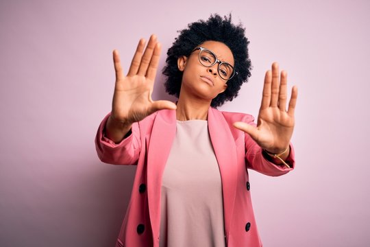 Young beautiful African American afro businesswoman with curly hair wearing pink jacket doing frame using hands palms and fingers, camera perspective