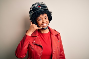 Young African American afro motorcyclist woman with curly hair wearing motorcycle helmet smiling doing phone gesture with hand and fingers like talking on the telephone. Communicating concepts.