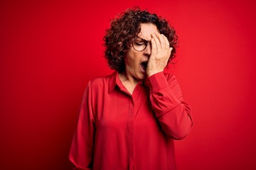 Fototapeta na wymiar Middle age beautiful curly hair woman wearing casual shirt and glasses over red background Yawning tired covering half face, eye and mouth with hand. Face hurts in pain.