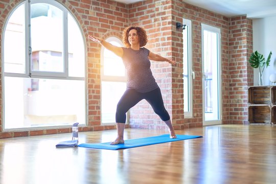 Middle age beautiful sportwoman smiling happy. Standing on mat practicing yoga doing warrior pose at gym
