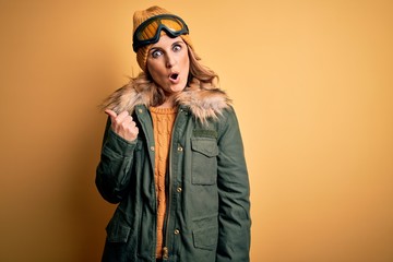 Middle age beautiful blonde skier woman wearing snow sportwear and ski goggles Surprised pointing with hand finger to the side, open mouth amazed expression.