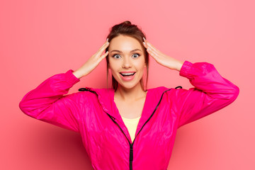 excited sportswoman touching head while looking at camera on pink background