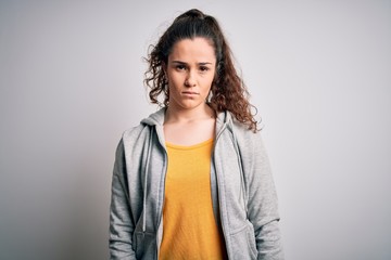 Young beautiful sportswoman with curly hair wearing sportswear over white background with serious expression on face. Simple and natural looking at the camera.