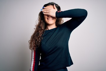 Young beautiful woman with curly hair wearing casual sweater over isolated white background smiling and laughing with hand on face covering eyes for surprise. Blind concept.