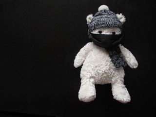 Soft toy polar bear in a black medical mask, hat and scarf on a black background. Kindergartens and schools are under quarantine. Home schooling