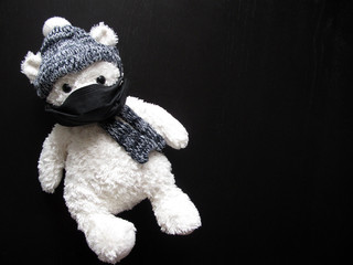 Soft toy polar bear in a black medical mask, hat and scarf on a black background. Kindergartens and schools are under quarantine. Home schooling