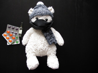 Soft toy polar bear in a black medical mask, hat and scarf with ampoule and tablets on a black background. Kindergartens and schools are under quarantine. Home schooling