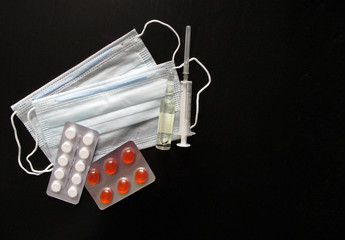 Medical masks with tablets, ampoule and syringe on a black background. Creating a vaccine against coronavirus. Covid19 virus, coronavirus and epidemic content. Copy space