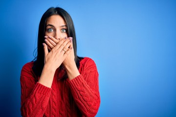 Young brunette woman with blue eyes wearing red casual sweater over isolated background shocked covering mouth with hands for mistake. Secret concept.