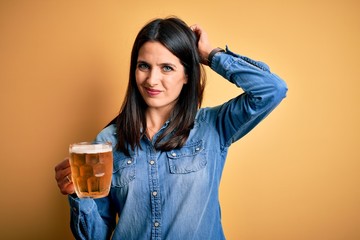 Young woman with blue eyes drinking jar of beer standing over isolated yellow background confuse...