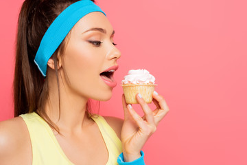 young sportswoman going to eat delicious cupcake with whipped cream isolated on pink
