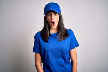 Young delivery woman with blue eyes wearing cap standing over blue background afraid and shocked with surprise expression, fear and excited face.