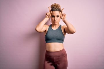 Young beautiful blonde sportswoman doing sport wearing sportswear over pink background doing funny...