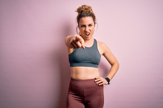 Young beautiful blonde sportswoman doing sport wearing sportswear over pink background pointing displeased and frustrated to the camera, angry and furious with you