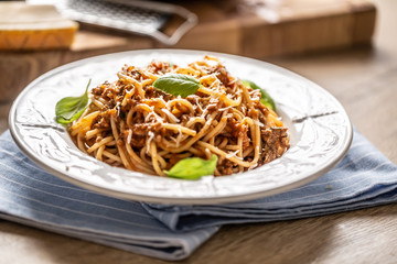 Italian pasta spaghetti bolognese served on white plate with parmesan cheese and basil