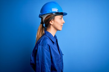 Young beautiful worker woman with blue eyes wearing security helmet and uniform looking to side, relax profile pose with natural face with confident smile.