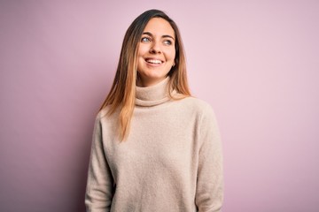 Obraz premium Beautiful blonde woman with blue eyes wearing turtleneck sweater over pink background looking away to side with smile on face, natural expression. Laughing confident.