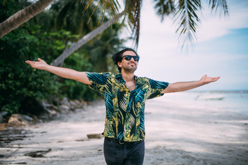 Beautiful man in a Hawaiian shirt walks on a tropical beach.