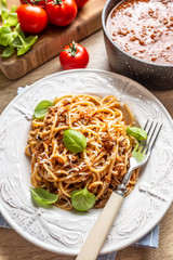 Italian pasta spaghetti bolognese served on white plate with parmesan cheese and basil