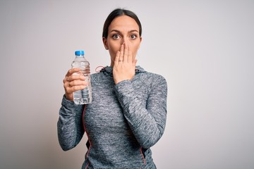 Young fitness woman wearing sport workout clothes drinking water from plastic bottle cover mouth with hand shocked with shame for mistake, expression of fear, scared in silence, secret concept