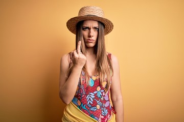 Young beautiful blonde woman wearing swimsuit and summer hat over yellow background Showing middle...