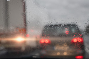 View from a car on a traffic jam on a rainy gloomy day, Raindrops on the glass in focus, commuters cars out of focus. Concept heavy urban traffic.