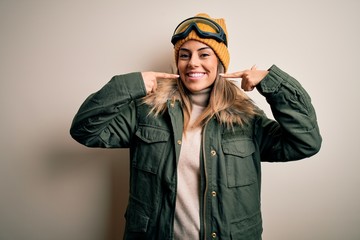 Young brunette skier woman wearing snow clothes and ski goggles over white background smiling cheerful showing and pointing with fingers teeth and mouth. Dental health concept.