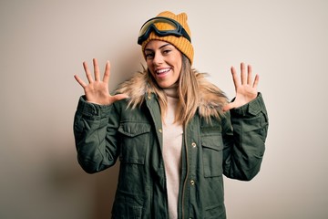 Young brunette skier woman wearing snow clothes and ski goggles over white background showing and pointing up with fingers number ten while smiling confident and happy.
