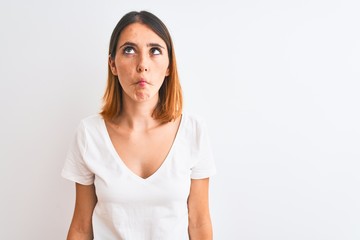 Fototapeta premium Beautiful redhead woman wearing casual white t-shirt over isolated background making fish face with lips, crazy and comical gesture. Funny expression.