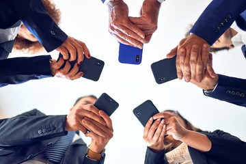 Group of business workers smiling happy and confident. Standing on a circle with smile on face using smartphone together at the office.