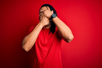 Young handsome african american afro man with dreadlocks wearing red casual t-shirt Covering eyes and mouth with hands, surprised and shocked. Hiding emotion