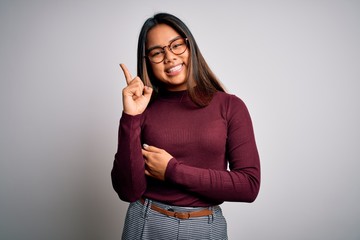 Beautiful asian business woman wearing casual sweater and glasses over white background with a big smile on face, pointing with hand and finger to the side looking at the camera.