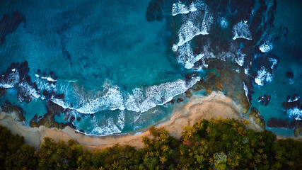 Scenic aerial shot of a sunny beach with white sand surrounded by transparent blue ocean water.