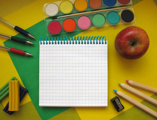 Fototapeta na wymiar Top view of school stationery: paints, colored pencils, pen, plasticine, notepad and apple on a background of colored paper. Back to school flat lay with copy space