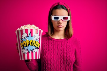 Obraz premium Young beautiful girl watching movie using 3d glasses eating box with popcorns skeptic and nervous, frowning upset because of problem. Negative person.